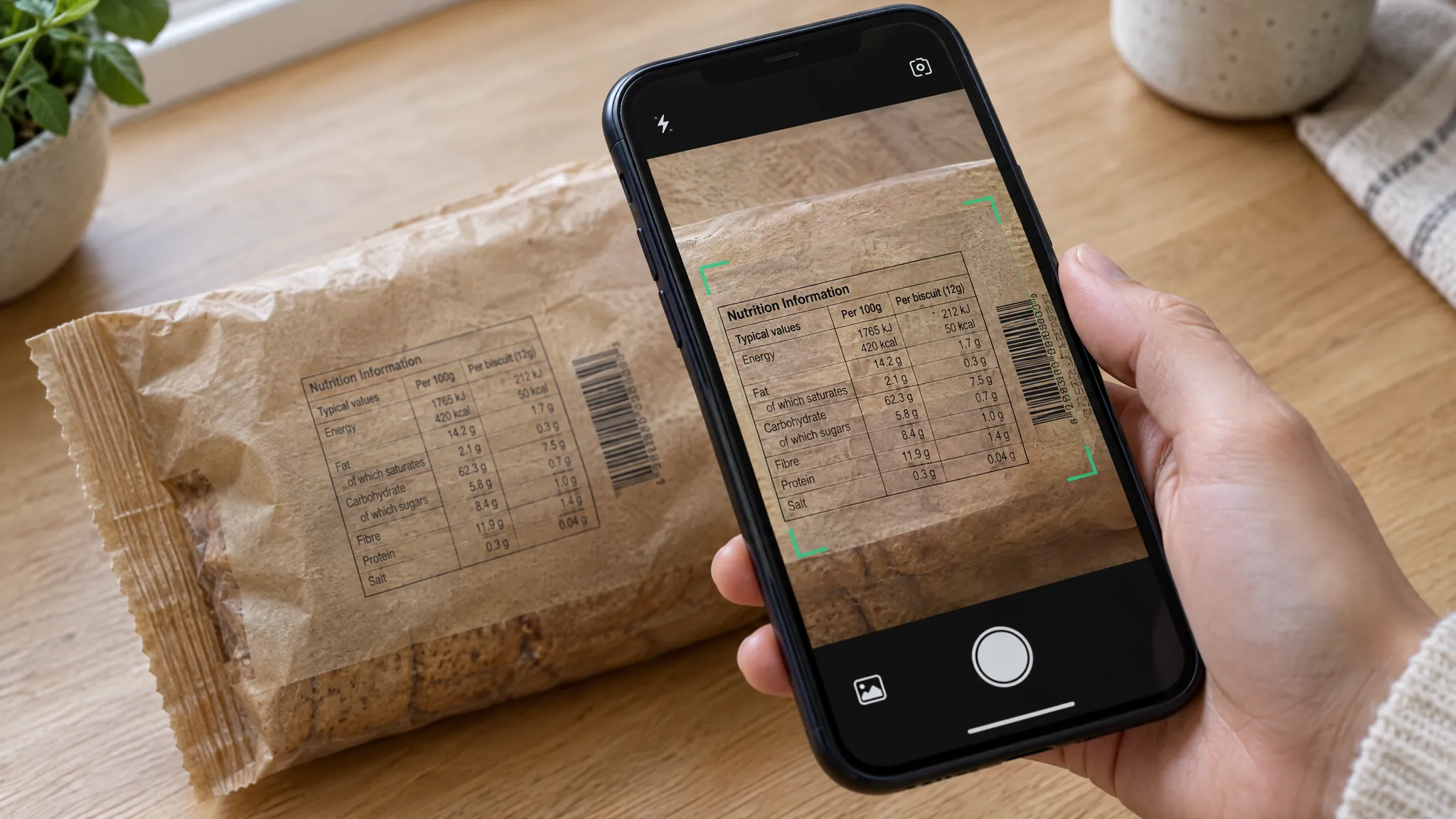 A phone held over the back of a packet of biscuits, with the nutrition information table and barcode framed on the screen.